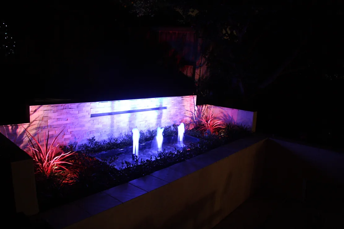 Colour-lit water-jet feature and sandstone wall at night